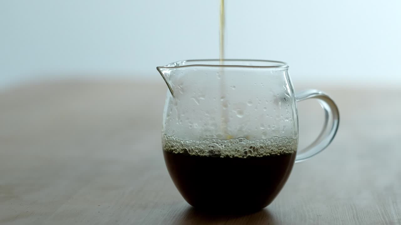 시네마그라프 - 색 바탕에 있는 테이블 위에 있는 투명한 컵에 신선한 커피를 부어줍니다.