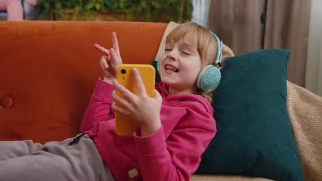 Niña-Relajada-Con-Auriculares-Escuchando-Música-Disco-Enérgica-En-Un-Teléfono-Inteligente-Tumbada-En-El-Sofá