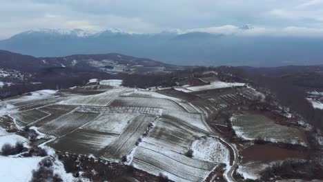 Antena-Sobre-Invierno-Llanuras-Montañosas-Cubiertas-De-Nieve-Brumoso-Día-Cambiante-Invierno-Nublado