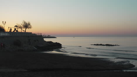 time-lapse video captures vibrant sunrise at coastline, with people leisurely strolling along the sandy shore