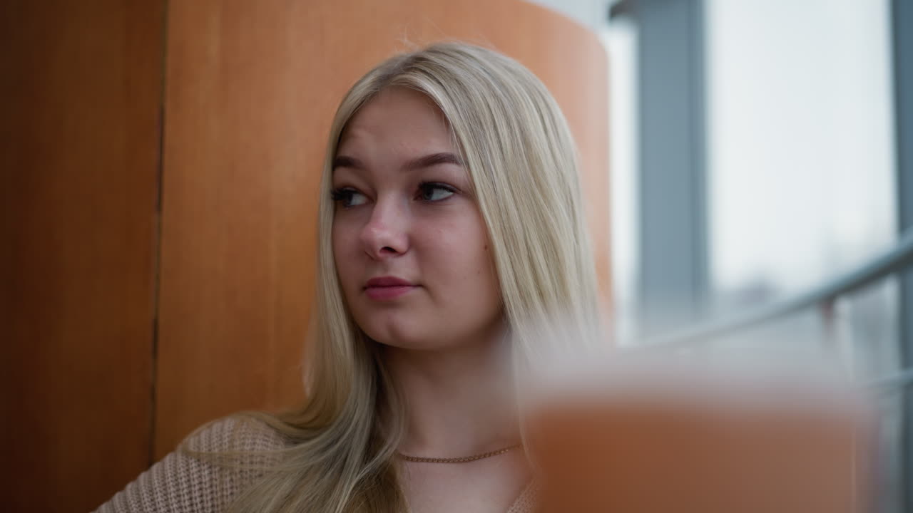 Russian lady sitting in mall looking contemplative around, possibly lost in thought or reflecting, with soft background blur of modern architecture and indoor setting