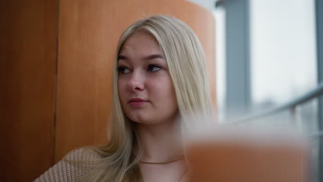 russian lady sitting in mall looking contemplative around, possibly lost in thought or reflecting, with soft background blur of modern architecture and indoor setting