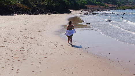 aerial view following a woman walking on a quiet beach, sunny day in india