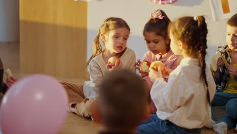 Preschool-children-sit-on-the-floor-on-special-cushions-and-eat-apples-and-bananas-during-a-break.-During-lunch-in-a-preschool-club