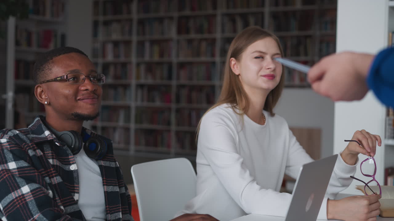 estudiantes satisfechos en una conferencia en la universidad. joven con gafas en las manos y chico negro compañero de grupo riendo escuchando al profesor en la biblioteca de la universidad
