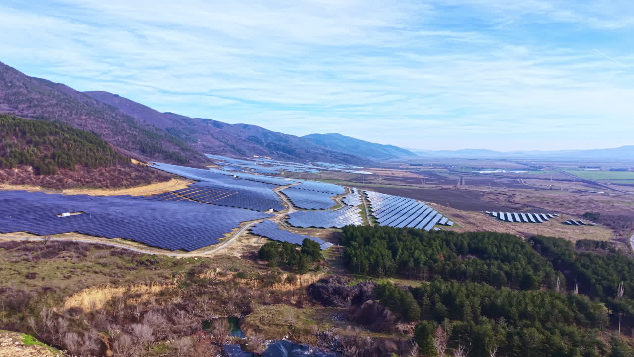 Solární panely pokrývají krajinu ve venkovské oblasti s horami a poli, znázorňující udržitelné energetické řešení a zemědělské využití po celý den.