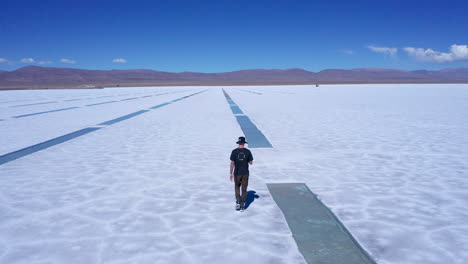 young man walks by extracted rows of salt at salt flats in argentina