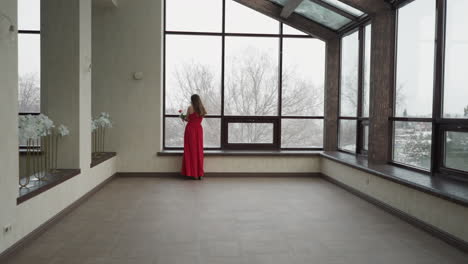 pensive woman stands near terrace window. young woman brings aura of sophistication to art studio environment gracefully looking at winter landscape