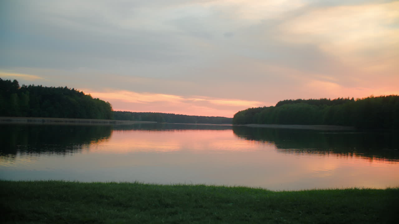 A man walking along the shore of a Polish lake at sunset. Colorful sky reflects on the water, creating a peaceful, scenic landscape filled with calm and natural beauty