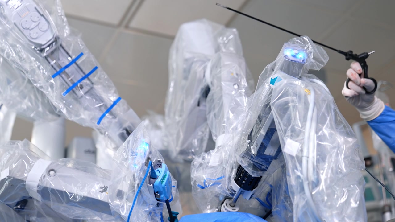 Doctor's hand with a modern medical tool device and arms of robotic surgeon coated in plastic. Minimally invasive surgery performed by Da Vinci machine.