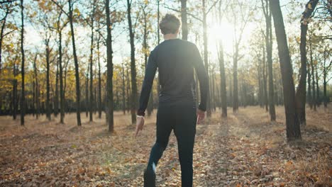 Rückansicht-Eines-Mannes-Mit-Lockigem-Haar-In-Einer-Schwarzen-Sportuniform,-Der-Sich-Vor-Dem-Start-Seines-Rennens-Am-Morgen-Im-Herbstwald-Aufwärmt.-Gesunde-Gewohnheiten-Und-Gesunder-Lebensstil:-Joggen-Am-Morgen