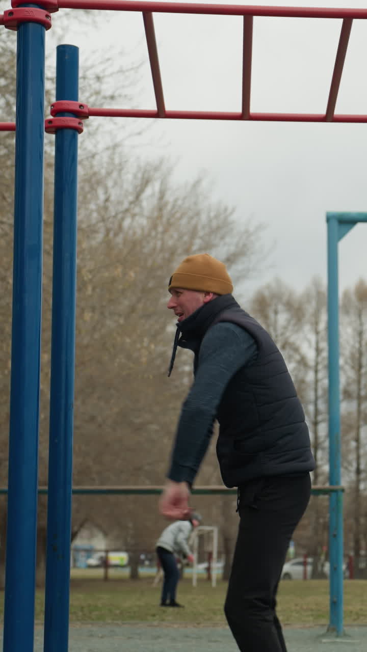 Close-up of a coach holding onto a red iron bar attached to blue poles, turning his body as he hangs and eventually drops down with a bounce