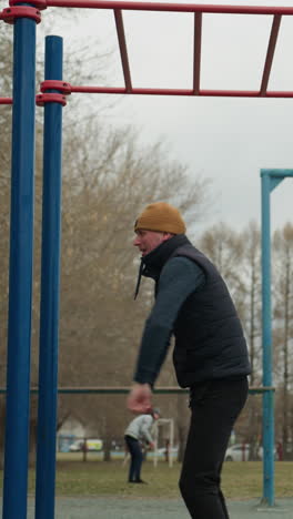 close-up of a coach holding onto a red iron bar attached to blue poles, turning his body as he hangs and eventually drops down with a bounce