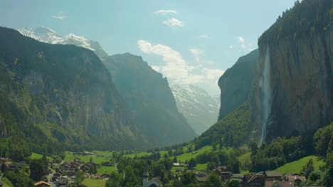 flying over town in scenic green valley with epic waterfall, switzerland