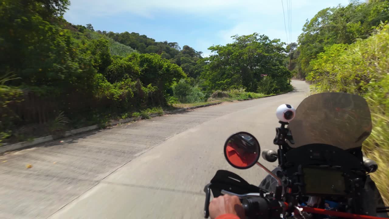 Experience the thrill of a motorbiker cruising along a winding coastal road surrounded by vibrant green forests. The ride captures the heart of nature's beauty.