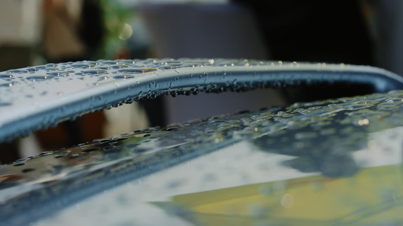 The close-up reveals the black car's surface adorned with large raindrops