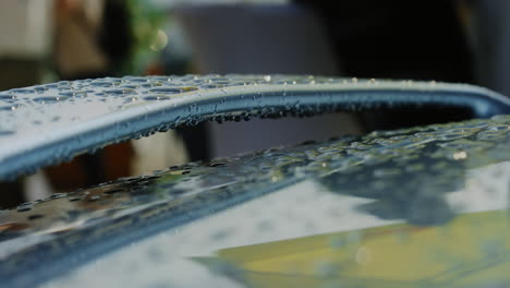 the close-up reveals the black car's surface adorned with large raindrops