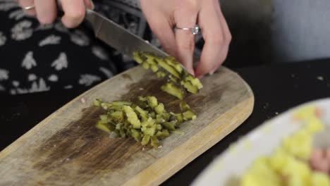 woman with sharp knife chop pickle into small cubes on wooden board