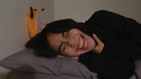 close-up shot of cute, asian girl with black hair in bed laughing uncontrollably