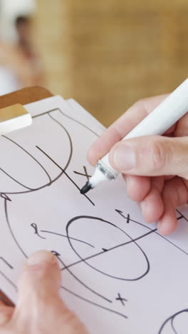 hands of basketball coach drawing diagram on clipboard