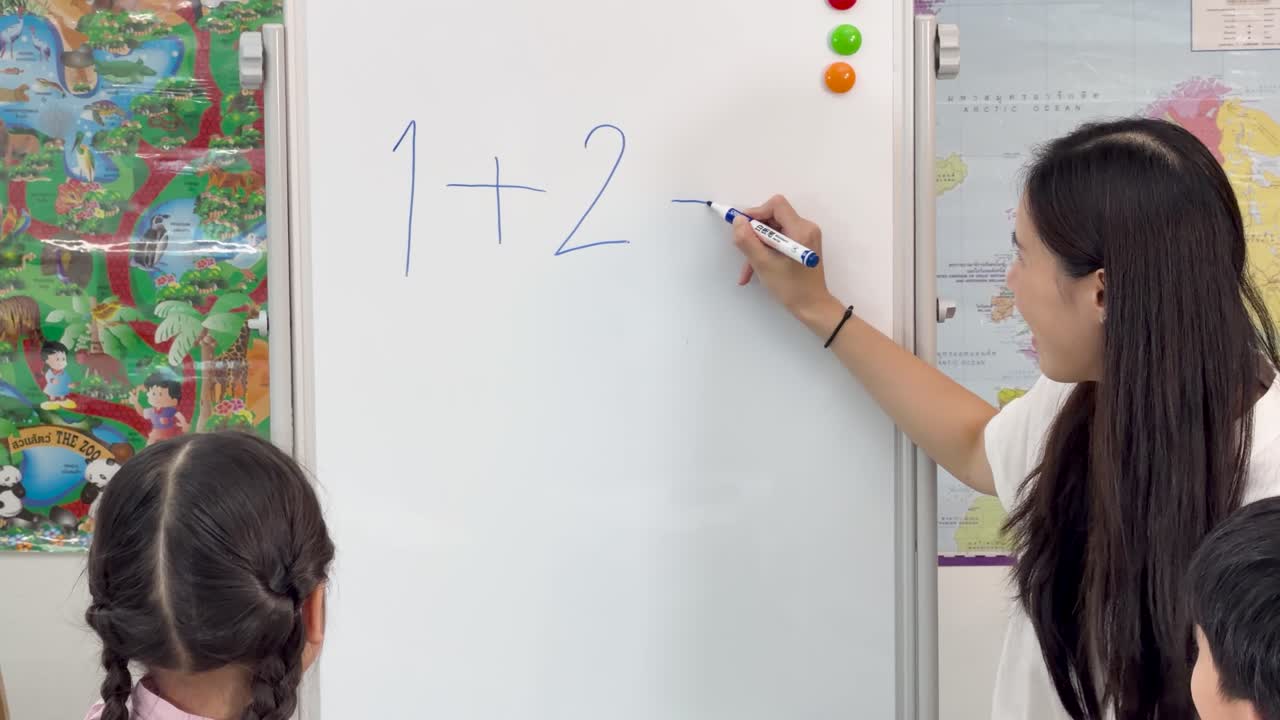 Female teacher guides young students through addition using whiteboard ...