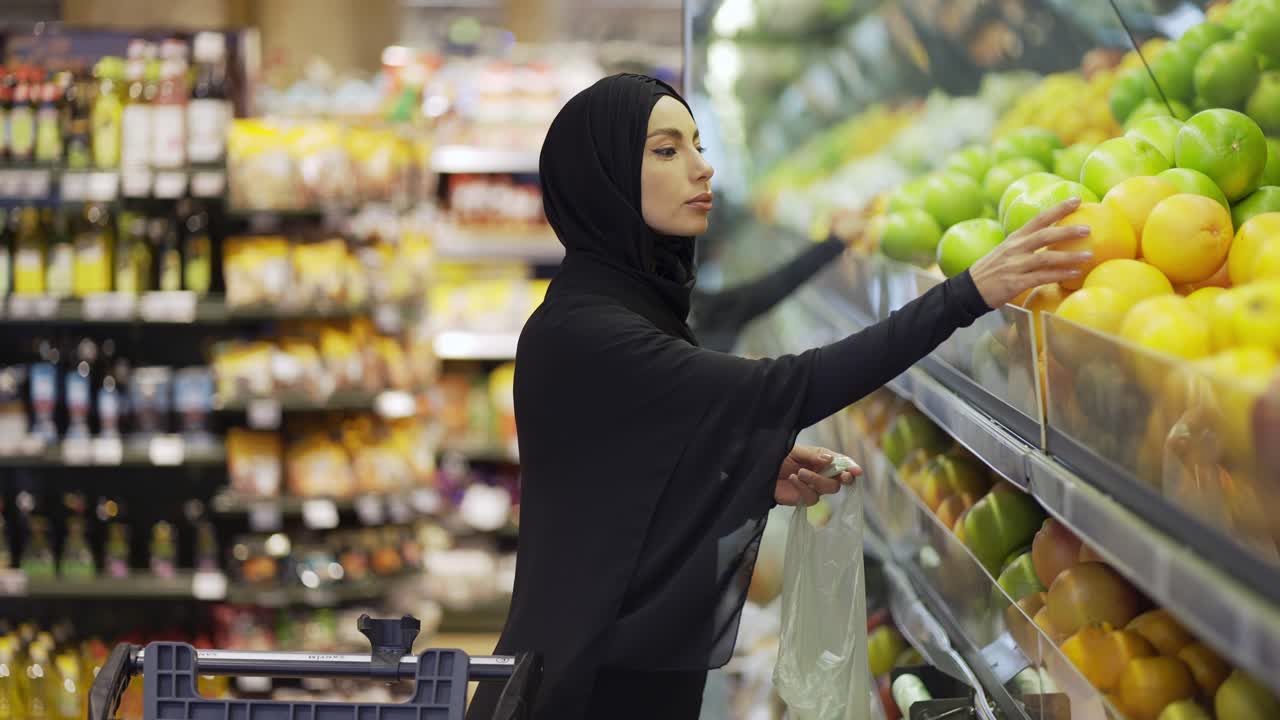 mujeres musulmanas comprando comestibles, tomando frutas de la estantería