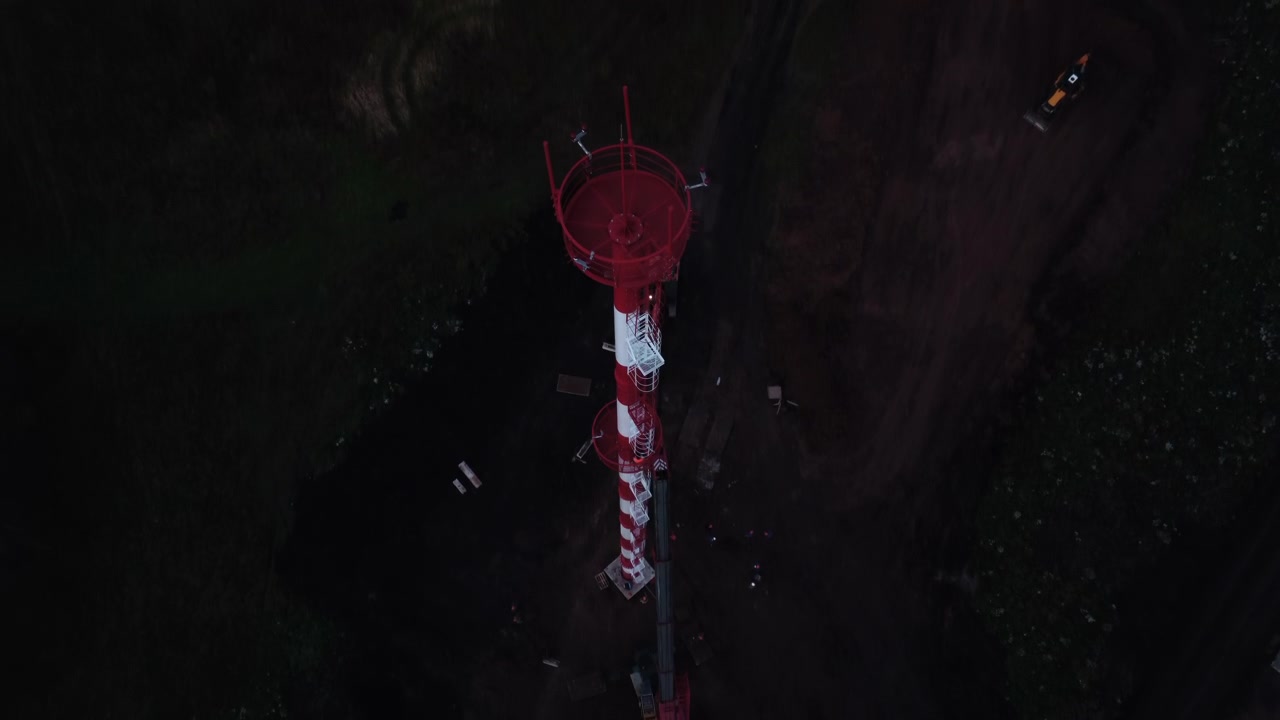 Vista dall'alto di una struttura offshore circolare rossa che galleggia in un mare scuro, con piccoli componenti circostanti e deboli riflessi superficiali in condizioni di scarsa illuminazione.