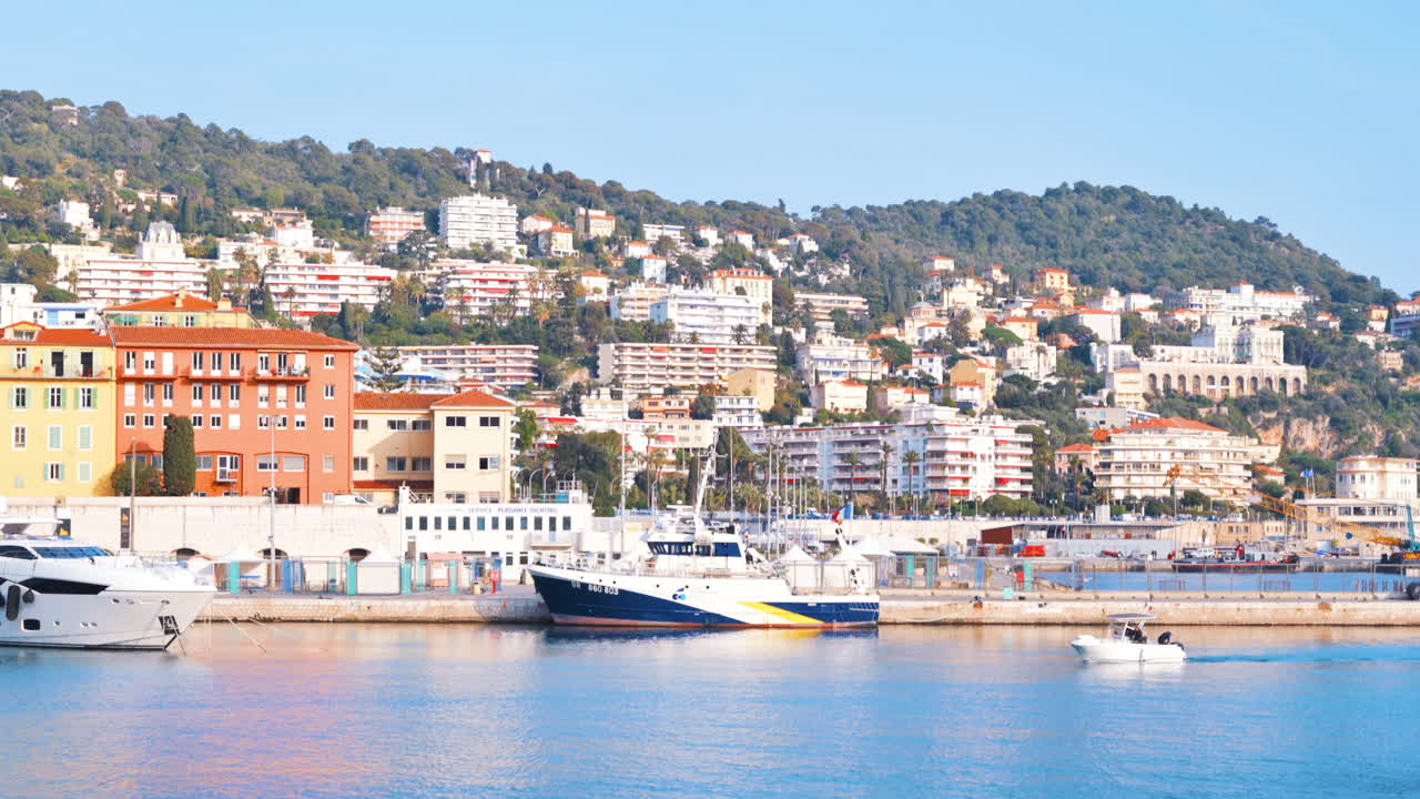 Barca bianca che si muove sul mare vicino a navi attraccate in un porto con vista sulla città di Nizza, Francia