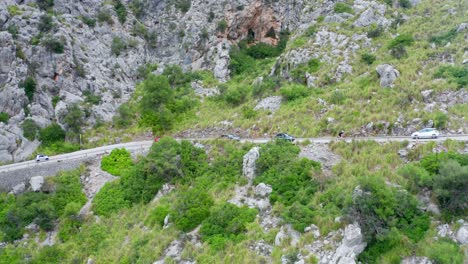 Cars-on-curvy-road-through-stony-green-mountain-range,-drone-aerial