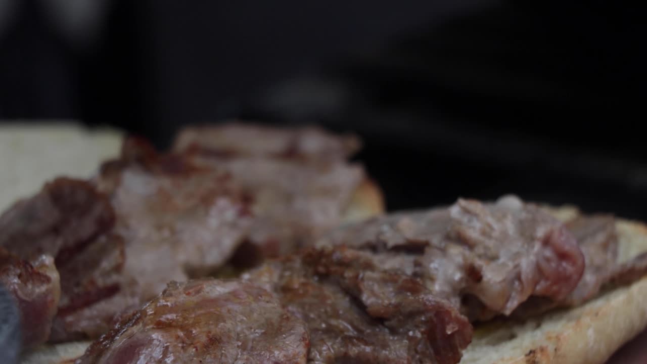 Chef places cut pieces of meat over a white piece of bread sandwich