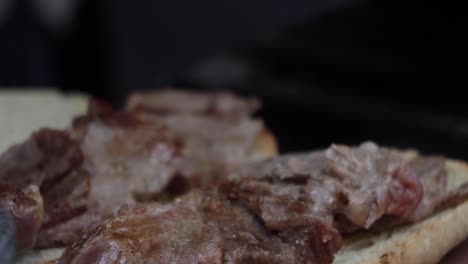 chef places cut pieces of meat over a white piece of bread sandwich