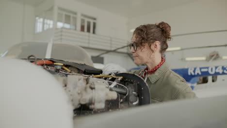 female technician fixing airplane engine with wrench in hangar