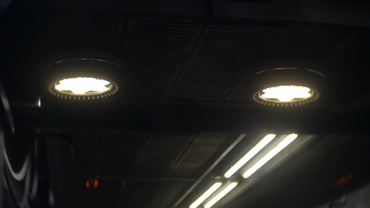 Tuberías que se extienden horizontalmente a través de una pared de hormigón manchada, múltiples líneas de colores creando una red de servicios industriales organizada. Iluminación cenital cálida proyectando un brillo suave mientras el ángulo de la cámara resalta.