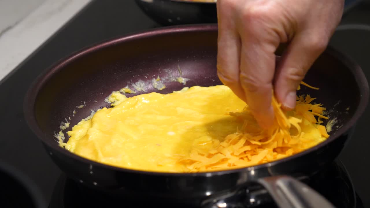 agregar queso cheddar rallado a la tortilla de huevo en una sartén - cocina