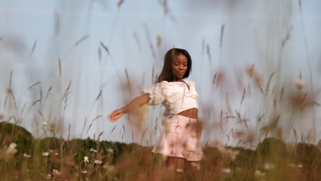 Black-woman-standing-in-flowery-field-posing-for-portrait-to-moving-camera-during-warm-sunny-day