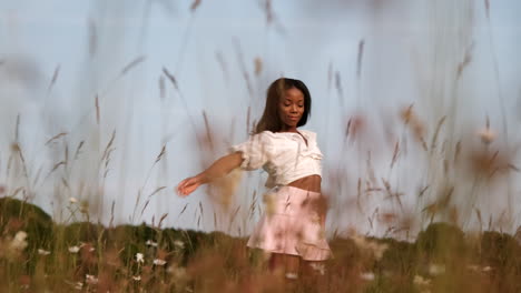 mujer negra de pie en un campo de flores posando para un retrato a la cámara en movimiento durante un cálido día soleado