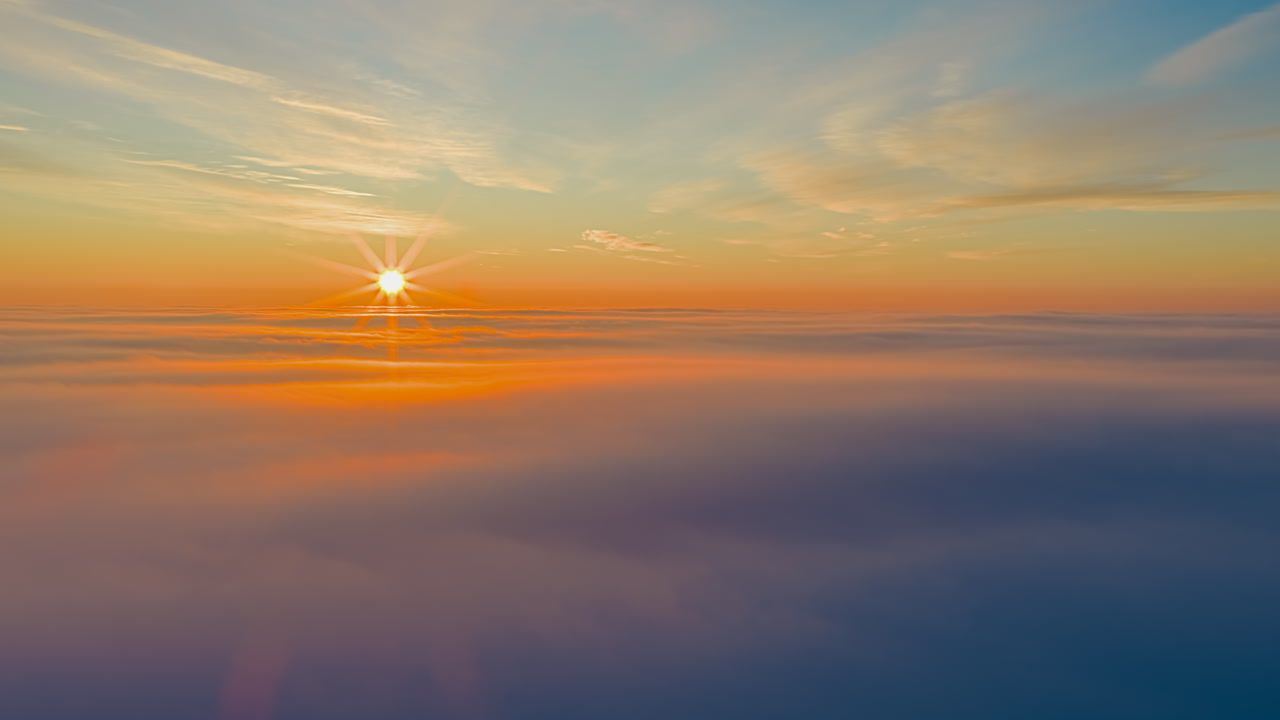 Breathtaking aerial footage of sun rising above thick cloud layer creating golden horizon and beautiful lens flares in blue sky high altitude flight