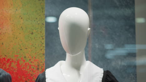 close-up of faceless mannequin dressed in black and white outfit displayed in storefront, with colorful textured background featuring red and green hues