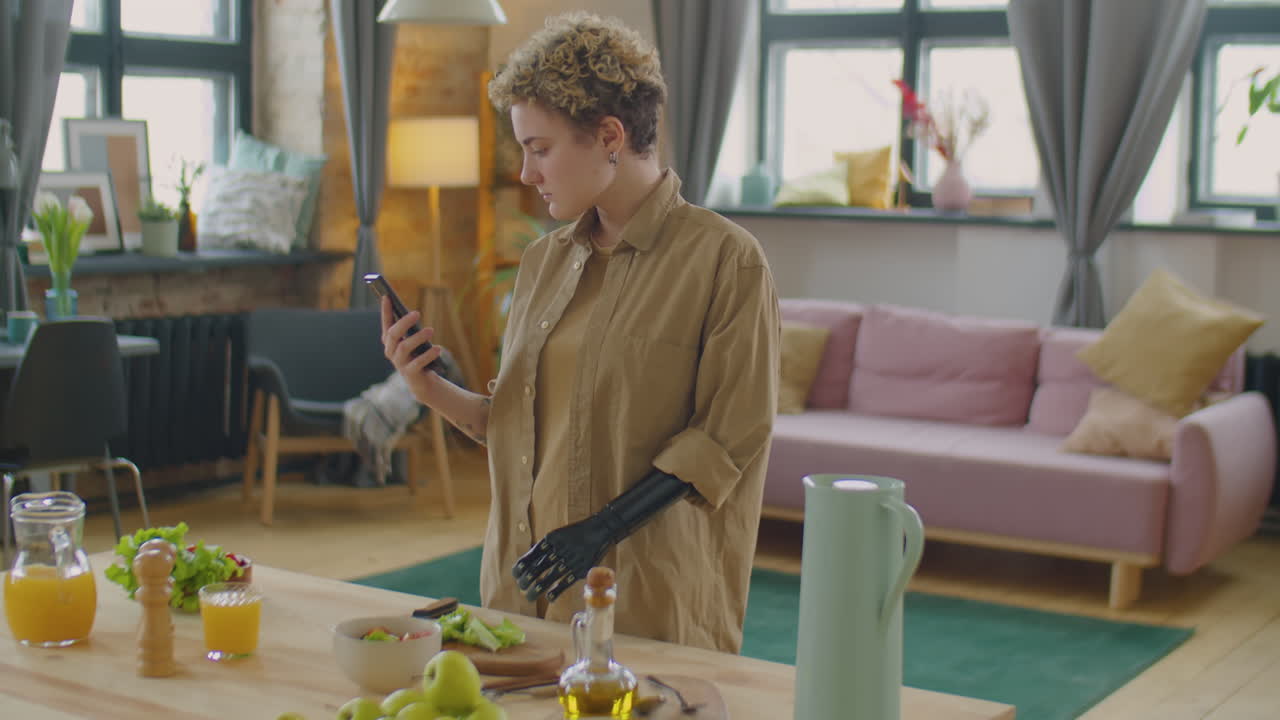 Girl with Prosthetic Arm Using Smartphone while Cooking Food