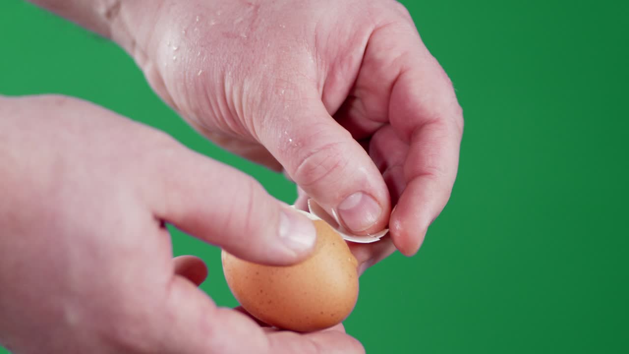 Men's hands clean a boiled egg from the shell.