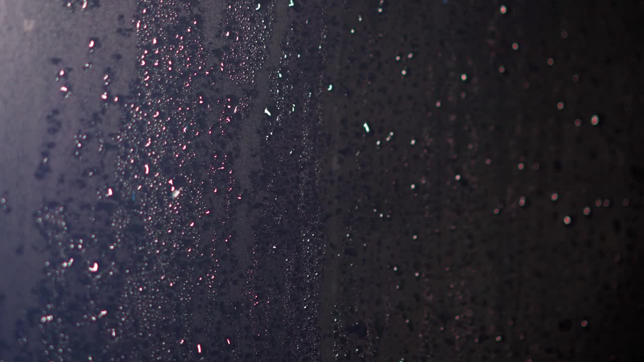 gotas de condensación en ventanas de vidrio debido a la lluvia iluminada con reflejos coloridos en las gotas de lluvia