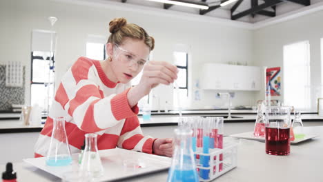 Conducting science experiment, young girl in school laboratory focused wearing safety goggles