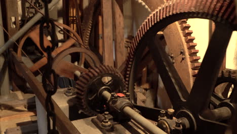 Spinning-metal-Gear-Wheels,-Cogwheels-in-wooden-Historical-old-Mill-,-warm-light-handheld-closeup-shot