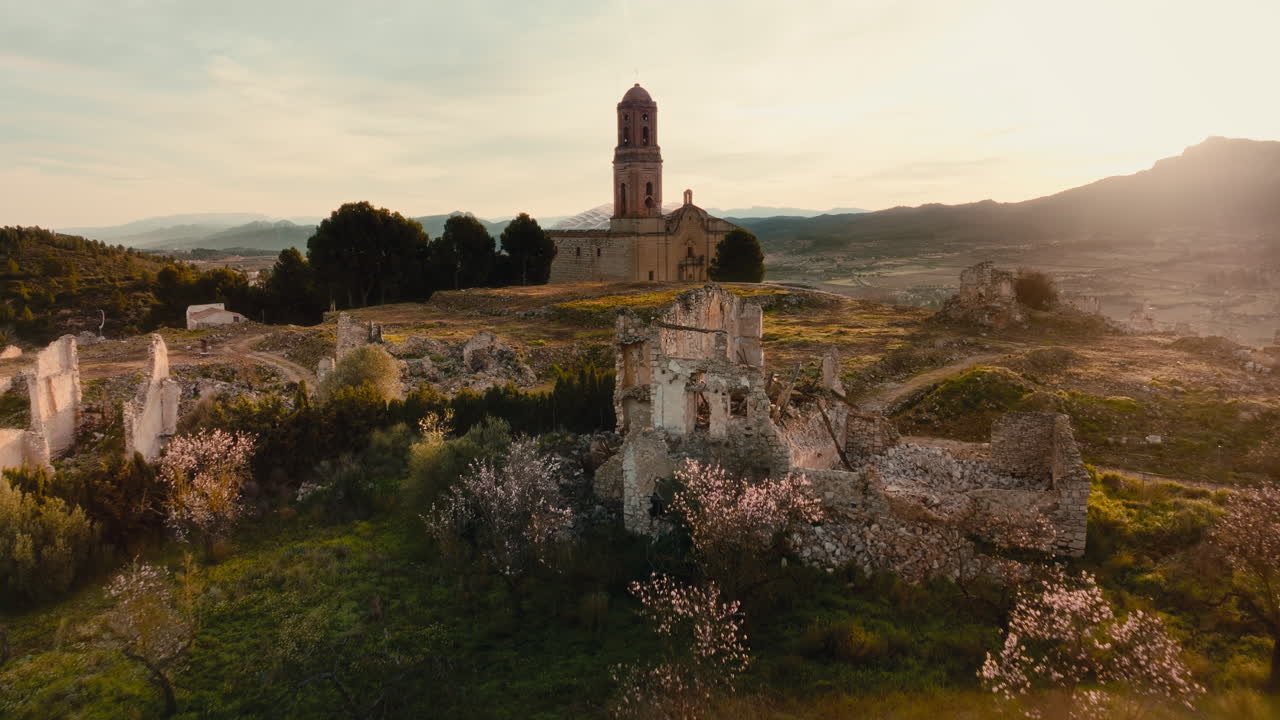 Cinematic 4K aerial drone shot slow push in toward setting sun over an abandoned hilltop town Corbera d'Ebre Spain, deserted after Spanish Civil War. Golden hour, historic church, dramatic landscape