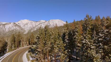 Antena-De-La-Carretera-Que-Serpentea-A-Través-Del-Lago-Tahoe-Con-Pan-Derecho-Al-Paisaje-De-Abetos-Douglas-Y-Montañas