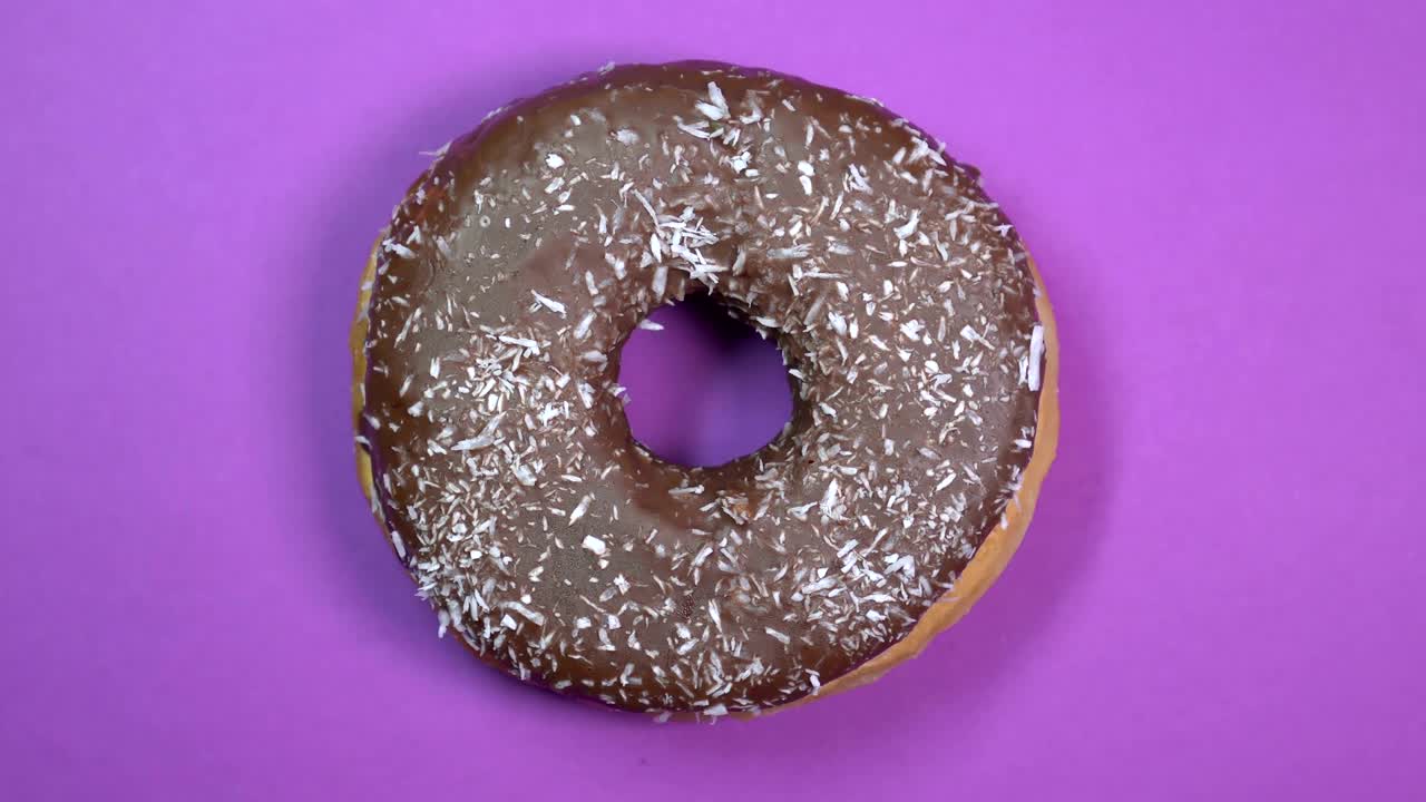 rosquilla de chocolate brillante y colorida con papas fritas de coco, tiro macro, girando sobre un fondo púrpura.