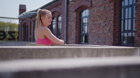 young blonde woman in pink workout clothes smiles by brick building