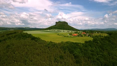 Drone-Vuela-Directamente-Sobre-Un-Río-Hacia-Una-Icónica-Formación-Rocosa-De-Montaña-En-Sajonia-Con-Cielos-Azules-Y-Nubes-En-Europa