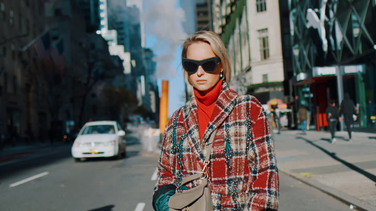 New York, USA, 5 ottobre 2025: Elegante donna bionda in posa su una strada di Manhattan in pieno giorno. Donna con cappotto a quadri e dolcevita rosso in piedi su una strada di New York City con sfondo urbano sfocato