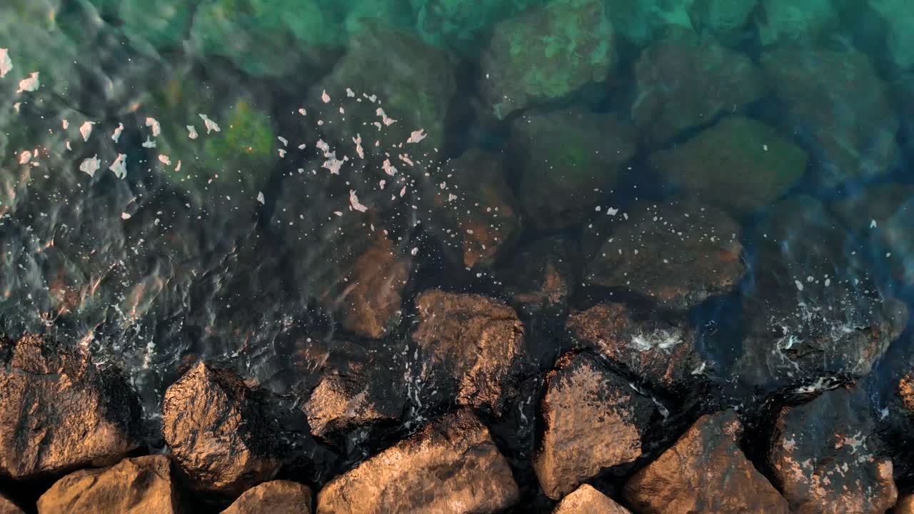 Drone ascends over reflective green turquoise shallow ocean waters with large rocks during the day, Aerial